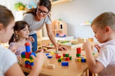 Preschool teacher with children playing with colorful wooden didactic toys at kindergarten