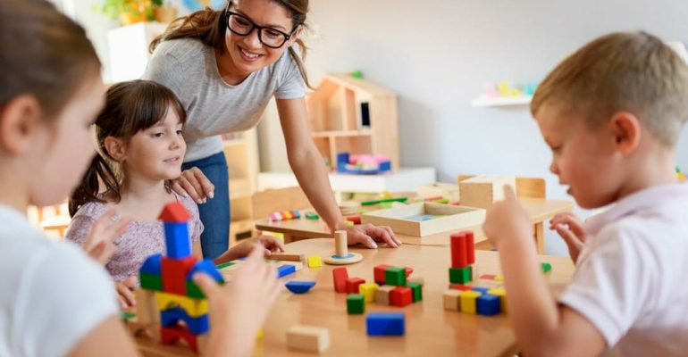 Preschool teacher with children playing with colorful wooden didactic toys at kindergarten